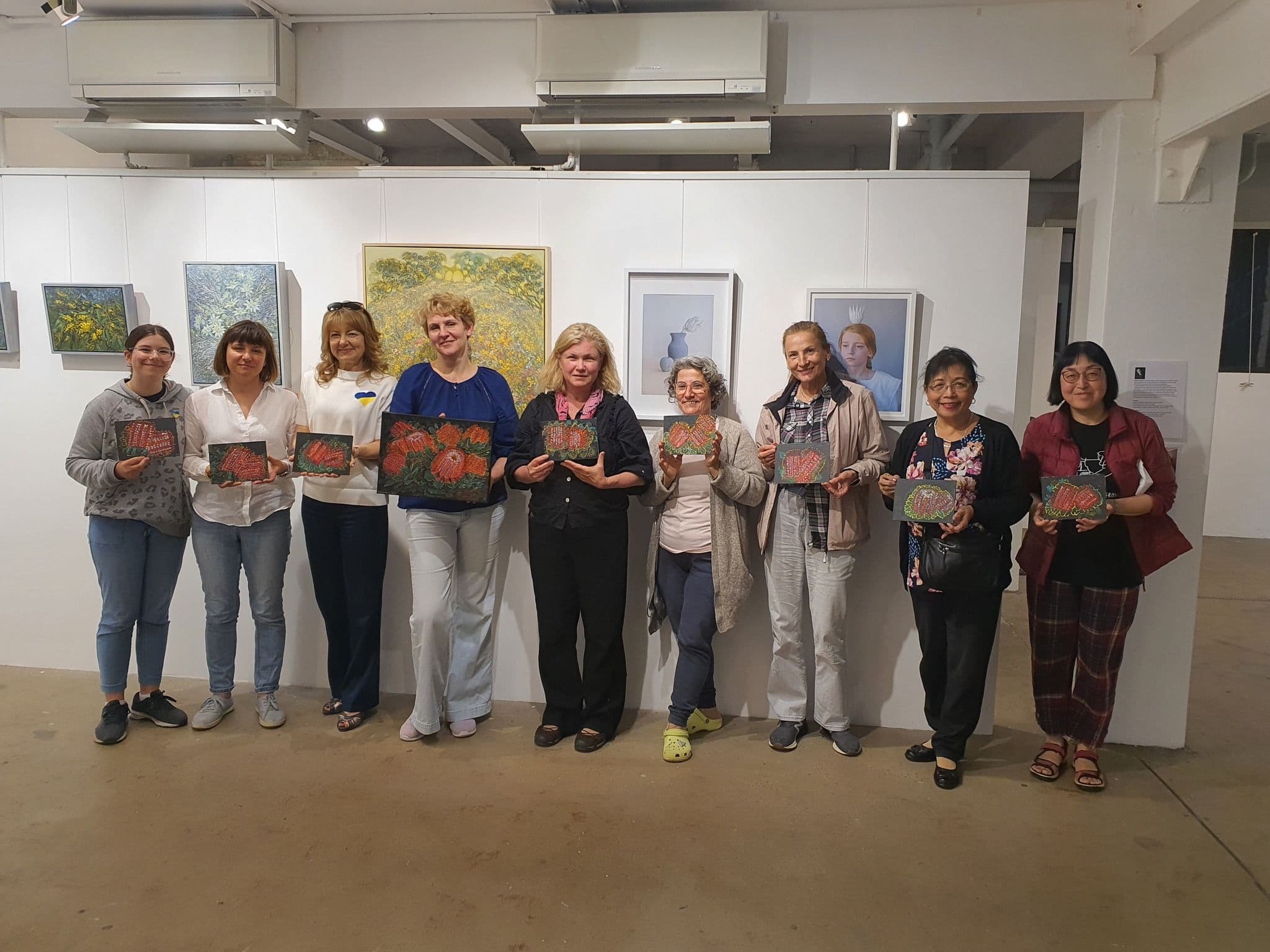 A large group of workshop participants at the exhibition holding their artworks