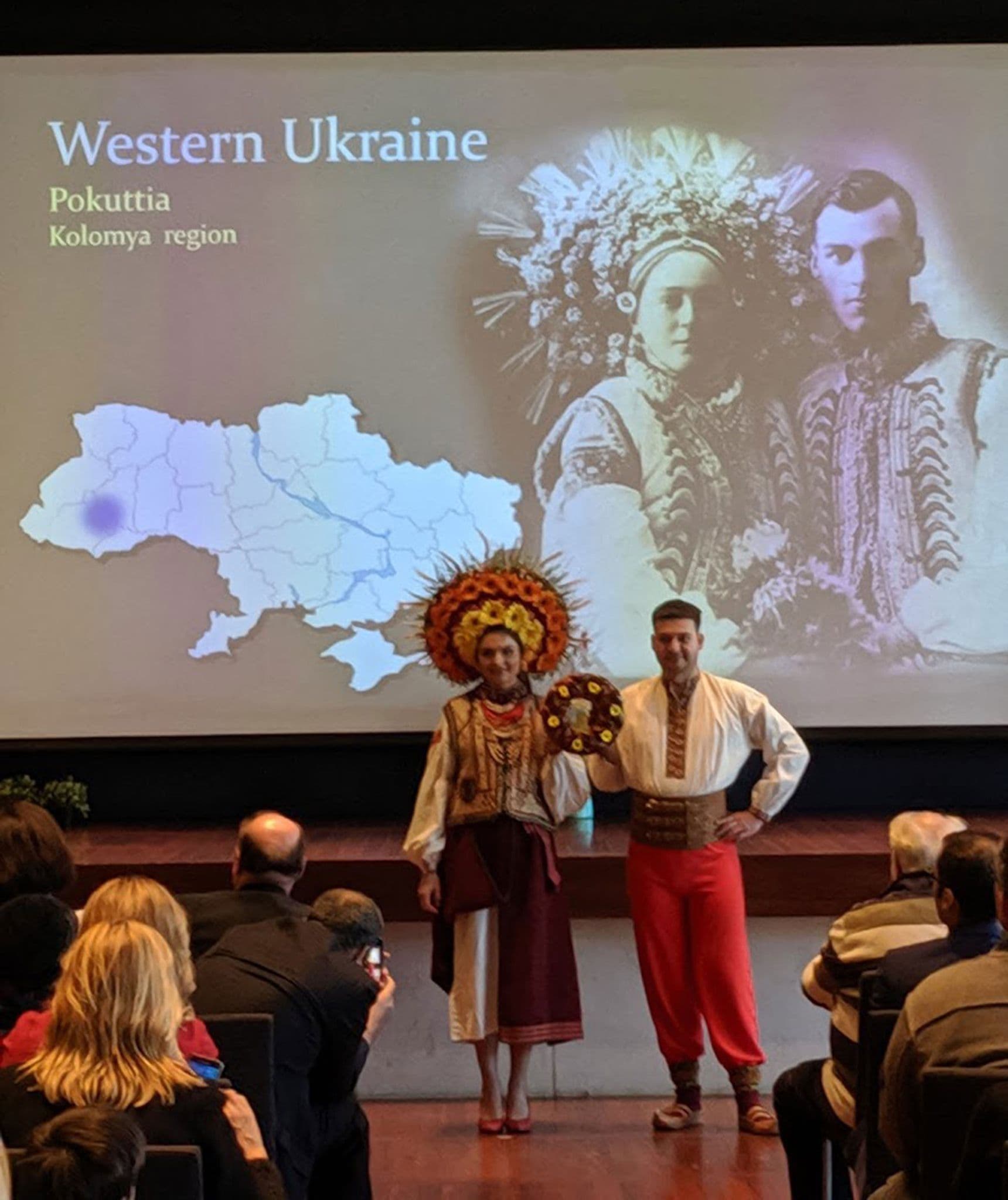 2 models in front of the large screen holding a ritual bread
