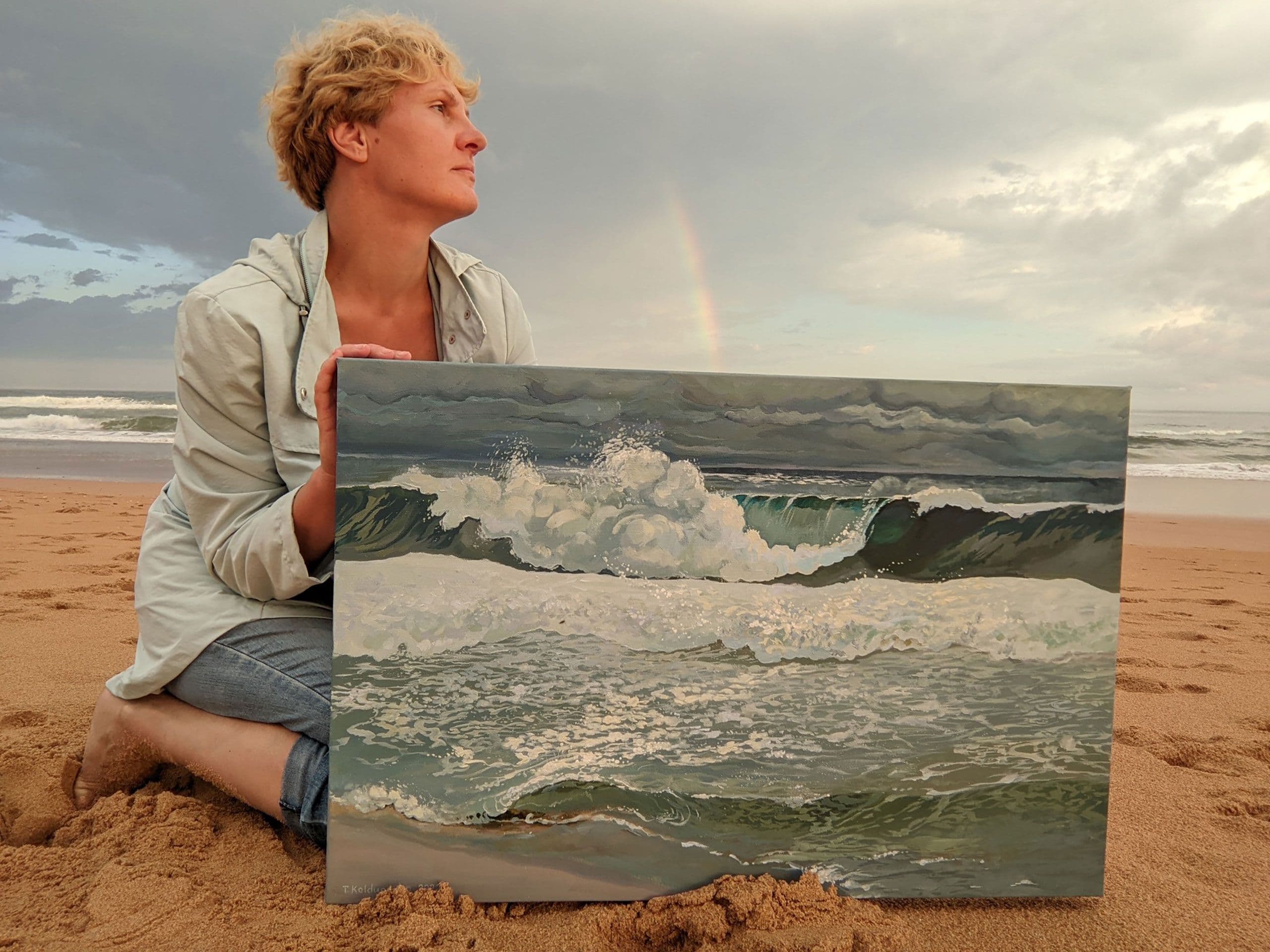 Tetiana Koldunenko holding her artwork A Glimpse of Hope sitting on the beach